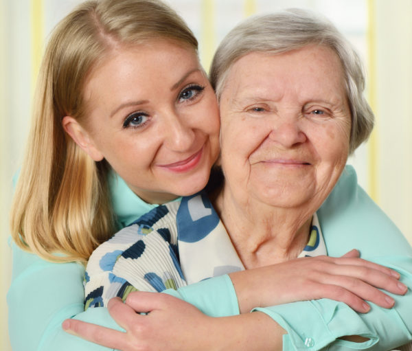 Caregiver hugging senior woman from behind
