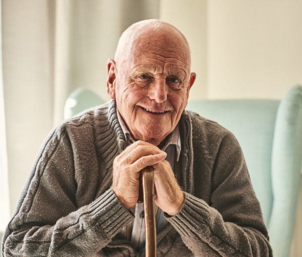 elderly man sitting on couch holding a cane